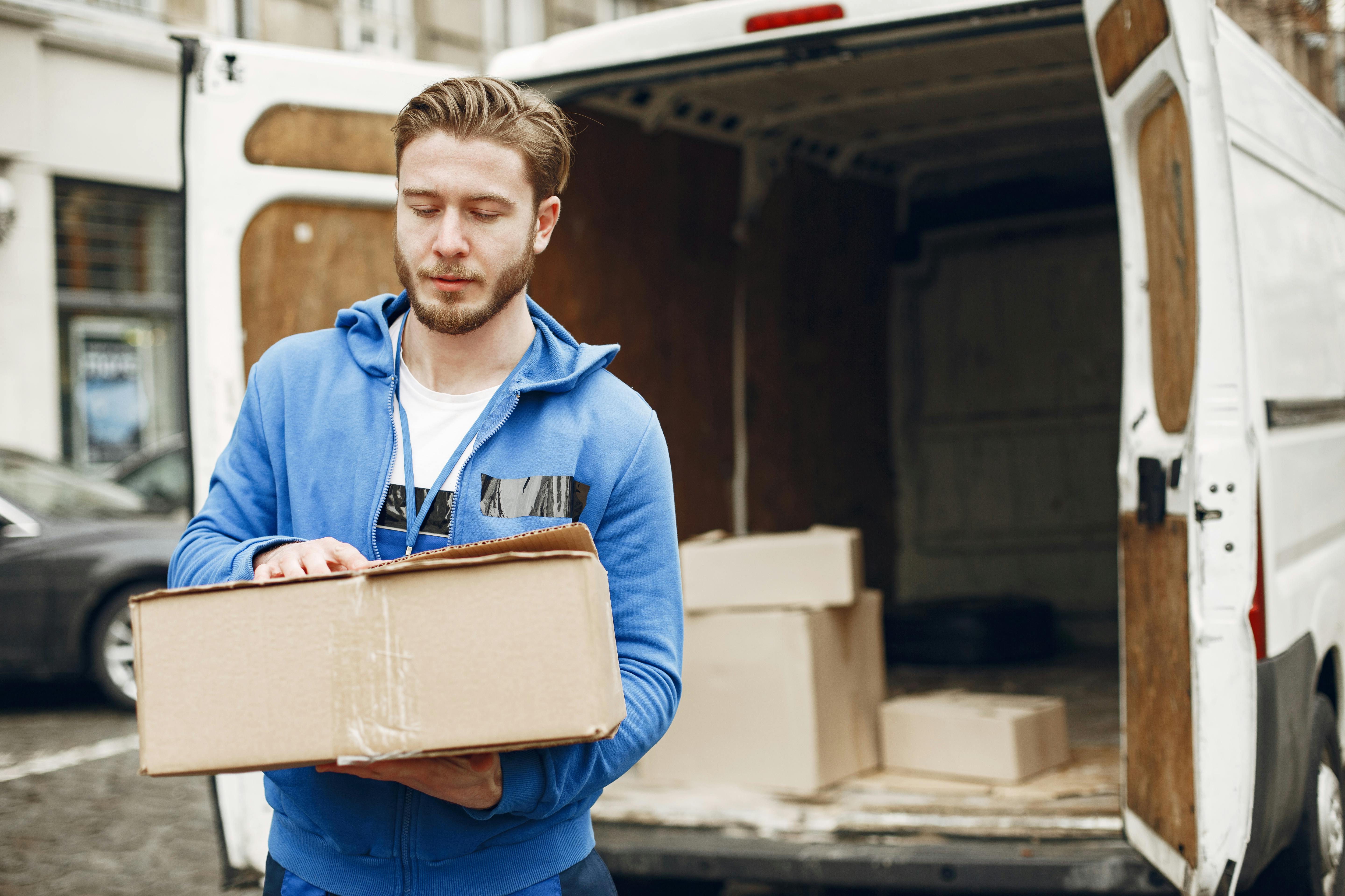 Mover carrying a cardboard box beside an open van