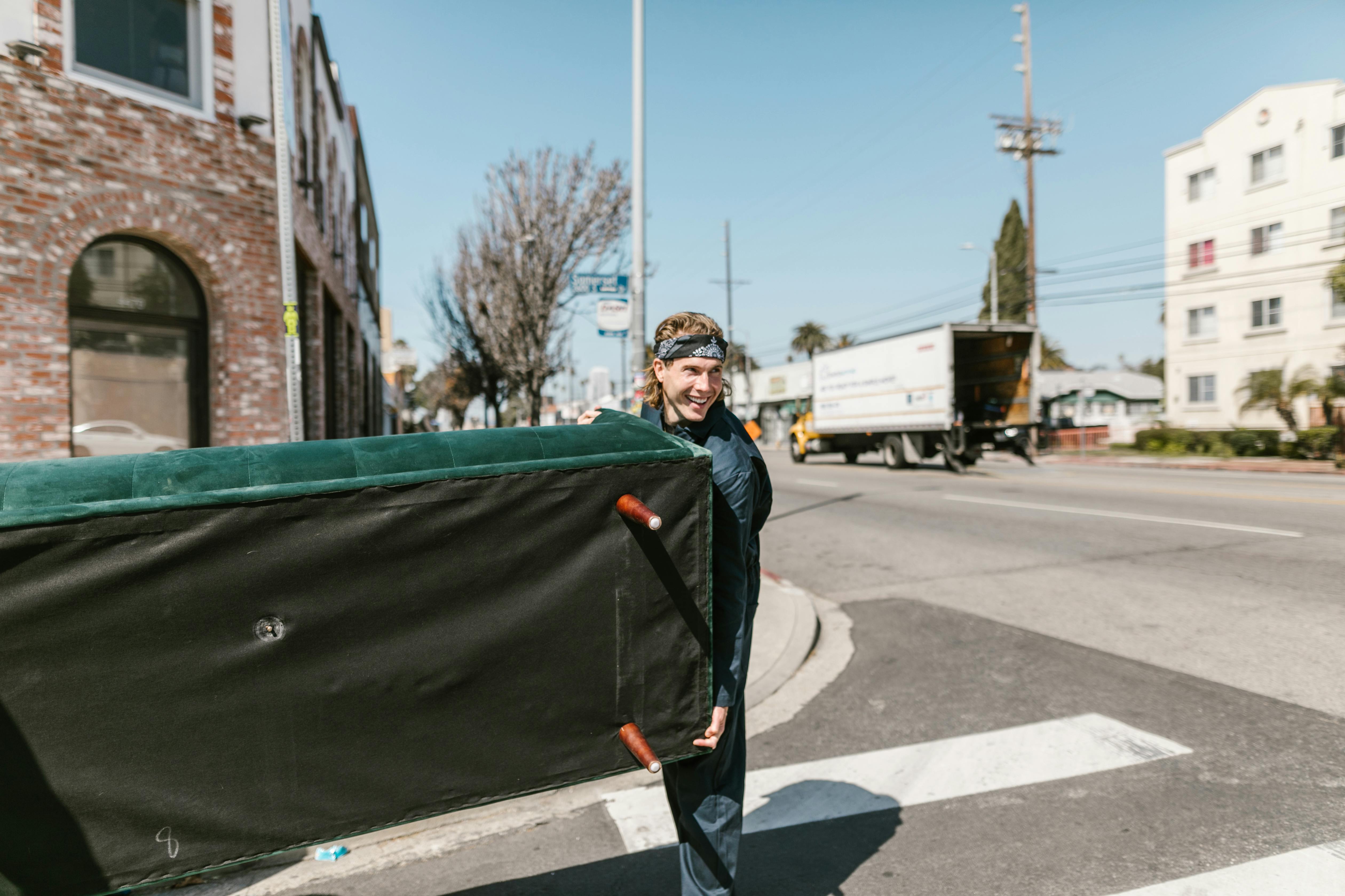 Mover carrying a wrapped piece of furniture across a street