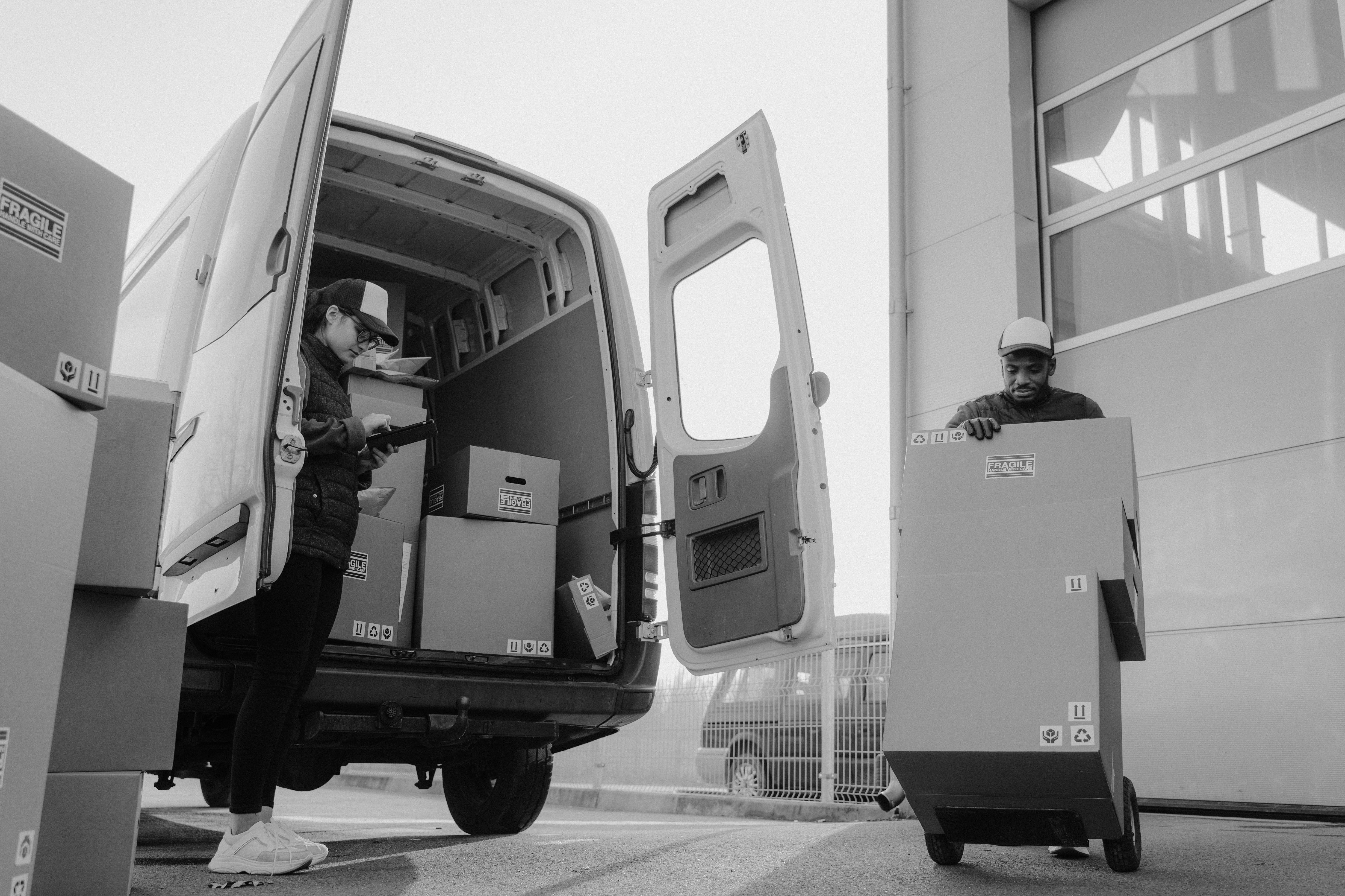 Black-and-white photo of a mover wheeling boxes on a hand truck beside a van